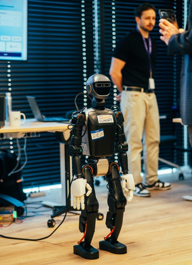 Humanoidalny robot Dex z logotypami DXC i Luxoft, prezentowany w strefie Experience Zone podczas konferencji AI Lab Day, ilustruje praktyczne i zaawansowane zastosowania technologii AI w automatyzacji procesów.