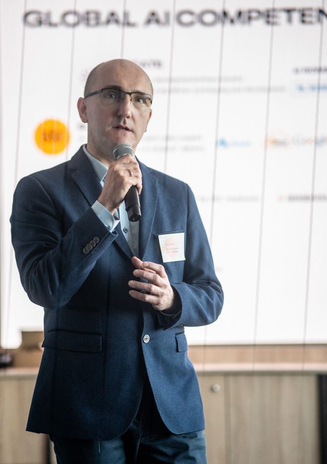 Michał Kowalczuk, Global AI Competency Center Director w DXC Technology Poland, przemawiający do mikrofonu podczas konferencji AI Lab Day poświęconej wdrażaniu strategii opartych na AI w przemyśle.